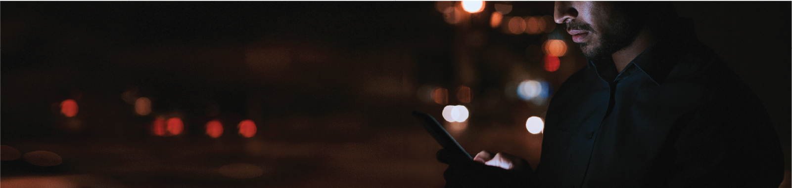 Photography of a man using a mobile device with bokeh lights in the background.