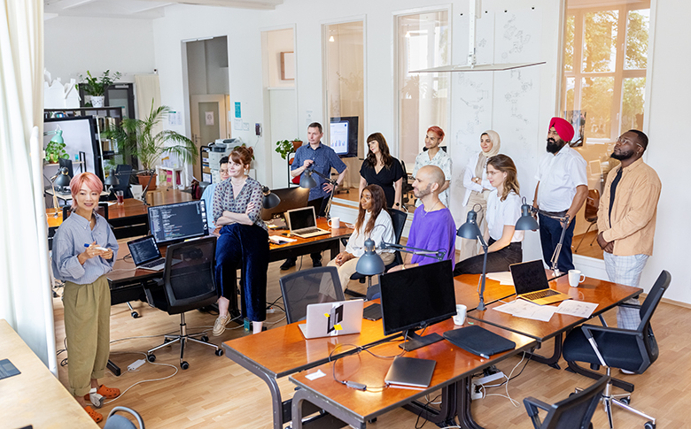 Photography of a group of international young people at an office standing and paying attention to a presentation.