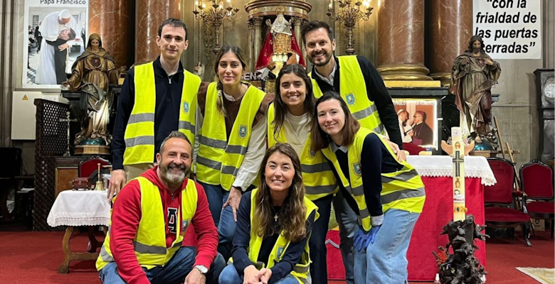 A group of seven individuals wearing yellow vests are inside a church, posing in front of a decorated altar, indicating their volunteer work in the community.