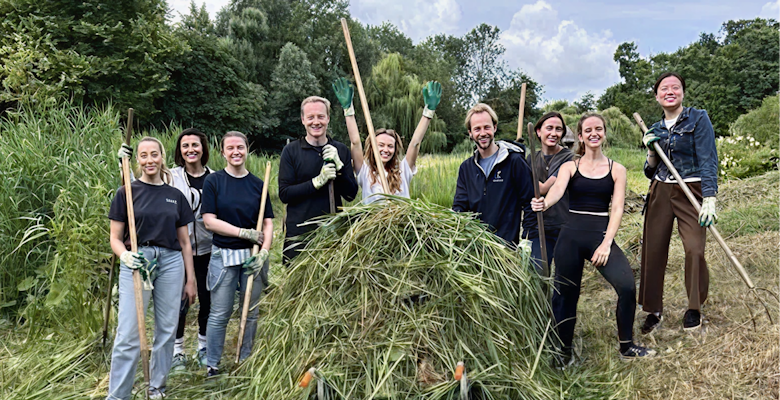A team of about eight people is shown in an outdoor setting, posing with tools used for clearing vegetation, demonstrating environmental conservation work.