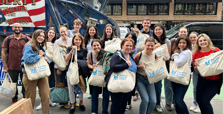 A group of approximately 16 individuals stands on a city street, holding canvas bags labeled "Rescuing Leftover Cuisine", in front of a garbage truck, showing participation in food rescue activities.