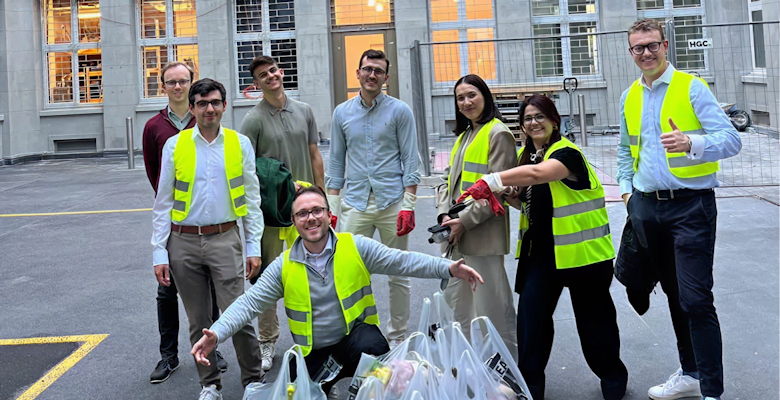 A group of eight people wearing bright yellow vests are gathered in a courtyard, posing with several garbage bags filled with waste, indicating teamwork in a community cleanup effort.