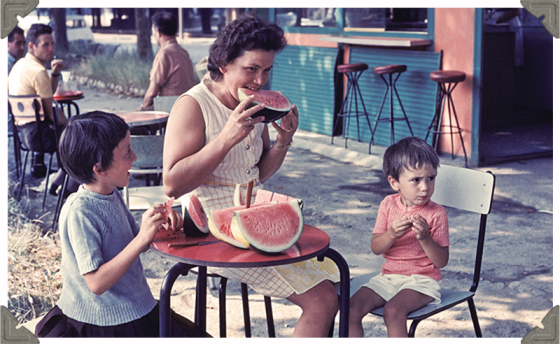 a picture of a woman with two children eating watermelon