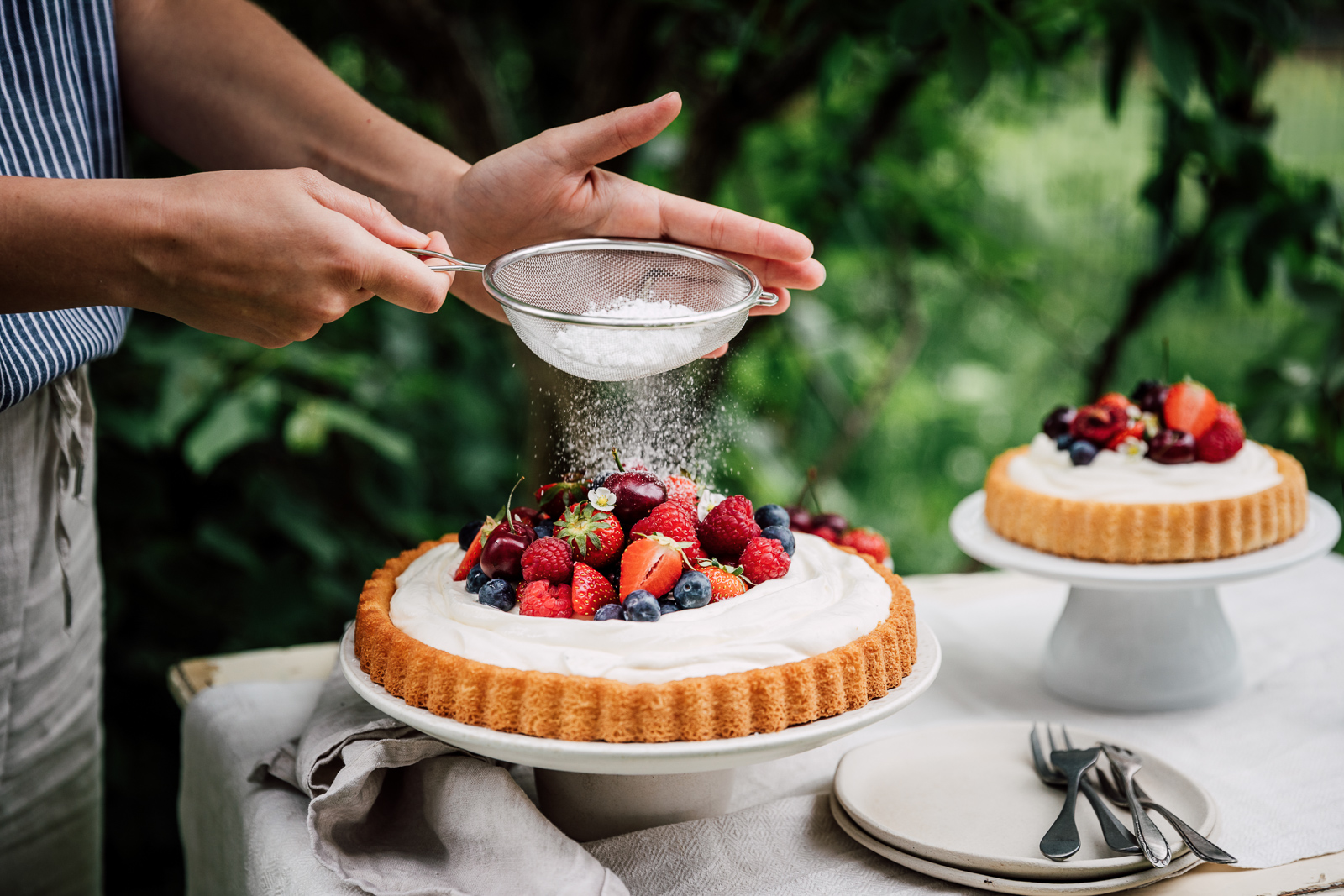 Person sprinkling sugar on top of fruit dessert