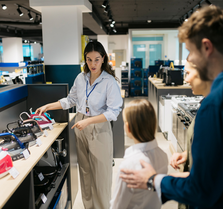 A sales associate demonstrates a variety of kitchen appliances to a parent and child in a modern electronics store.