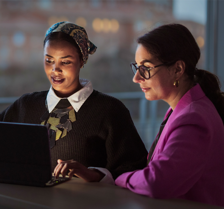 Photo of two women observing the screen of a laptop.