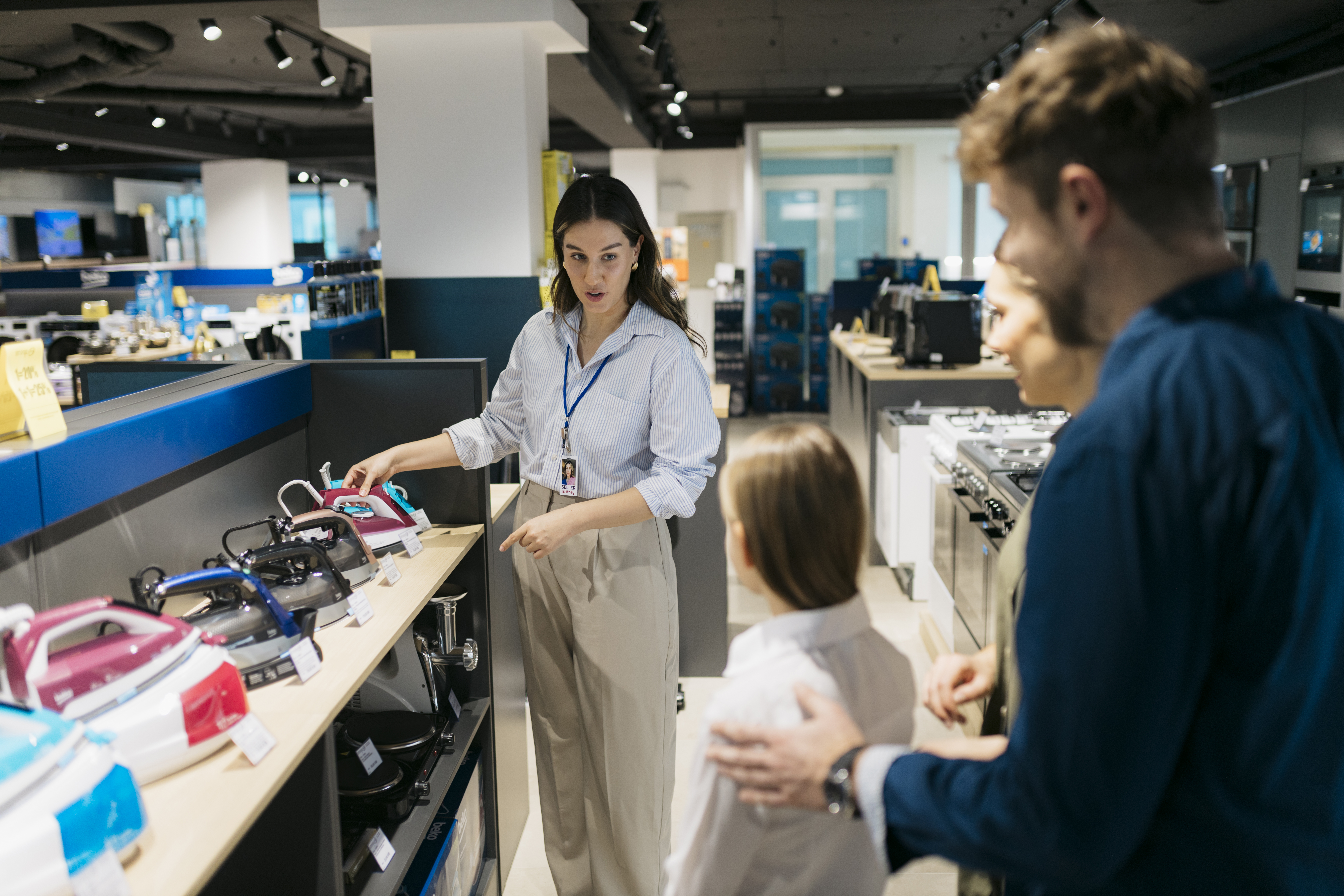 A sales associate demonstrates a variety of kitchen appliances to a parent and child in a modern electronics store.