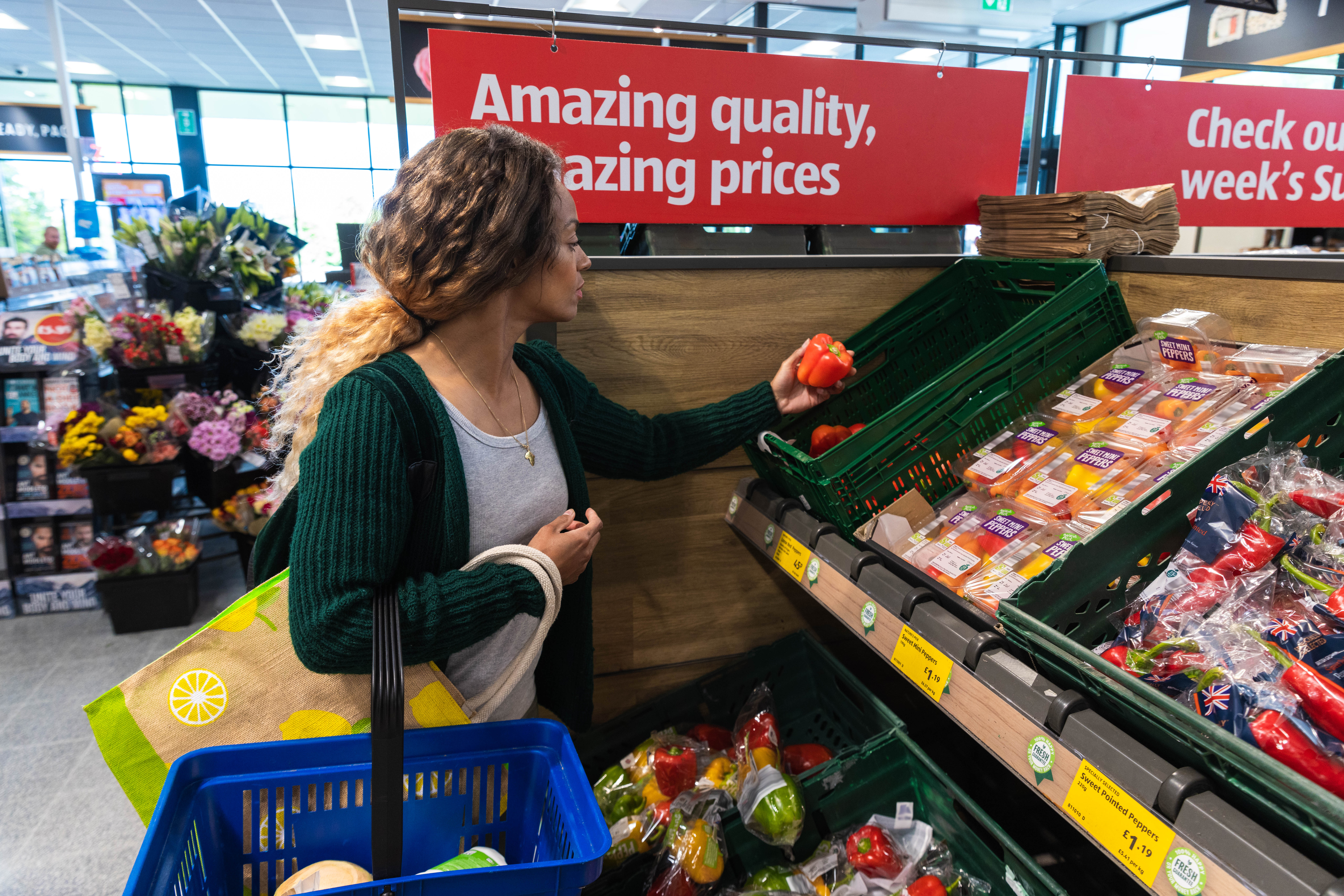 A shopper inspects colorful vegetables at a market, with a sign highlighting amazing quality and prices in the background.