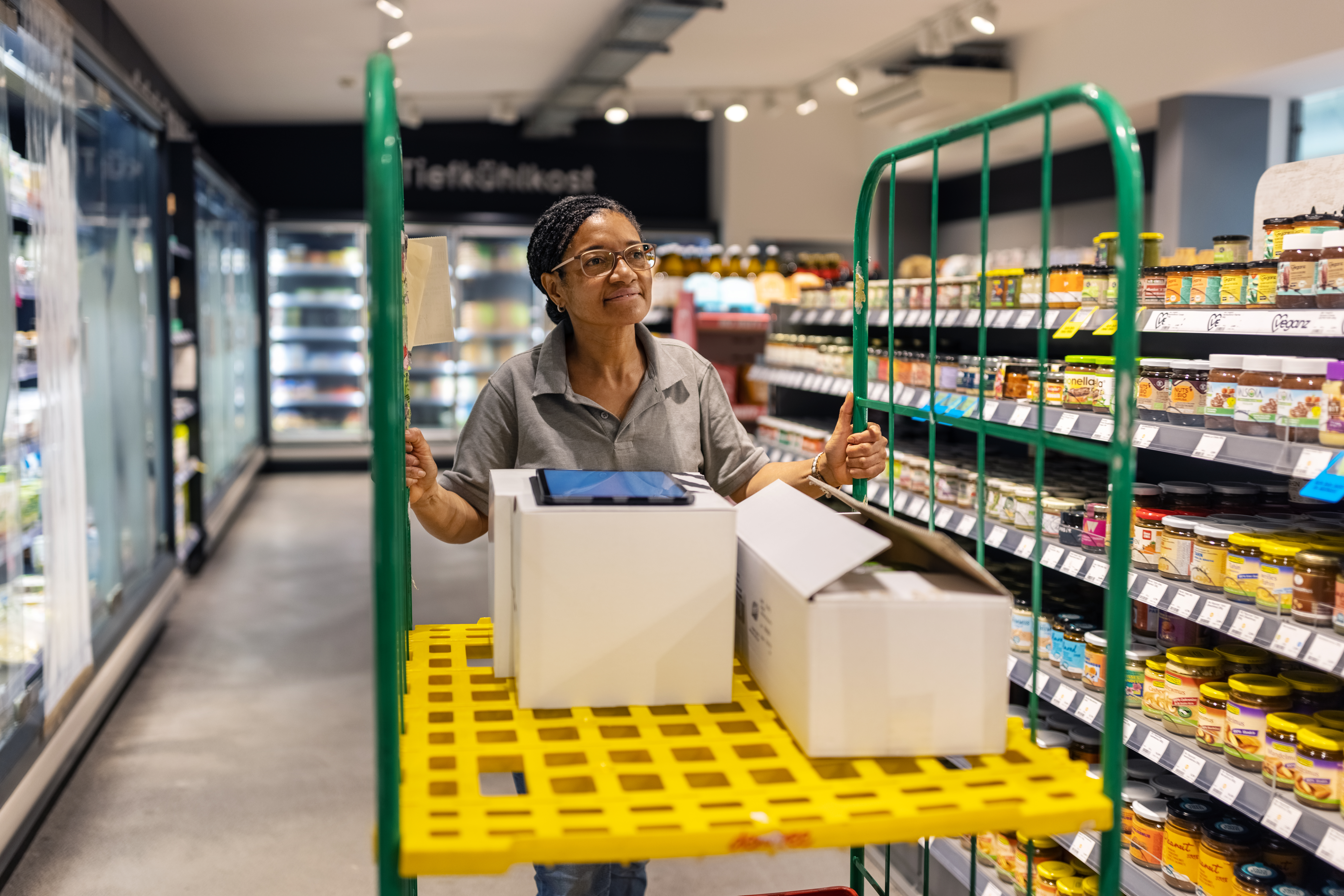 An individual pushing a trolley cart at grocer aisle refilling stocks